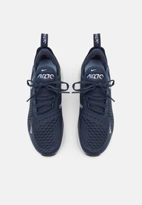 Marinblå sportskor med ett andningsbart mesh-överkant, snörningsdesign och semi-genomskinlig sula. Innehåller Nike-logotyp och ett strukturerat mönster.