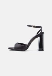 Melni satīna augstpapēžu sandales ar potītes siksniņu, atvērtu purngalu un spīdīgu bloka papēdi. Raksturo minimālas šuves un gludu tekstūru.
