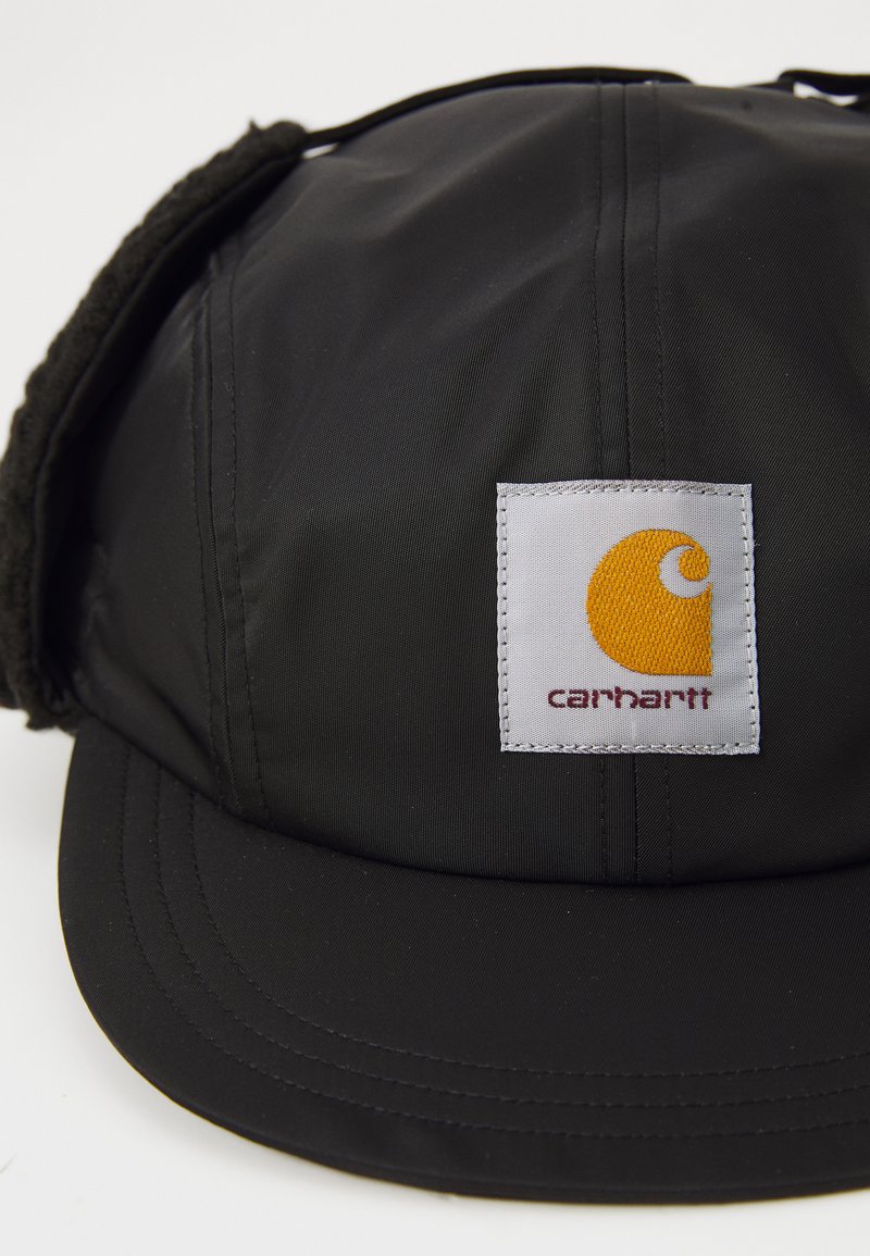 Zwarte pet van gestructureerd nylon met een platte klep, voorzien van een witte vierkante patch met een geel logo en de tekst "carhartt."