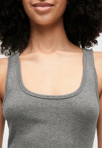 Siv špicast top s širokimi naramnicami in obrobnim izrezom, ki prikazuje mehak teksturiran material in oprijet kroj.