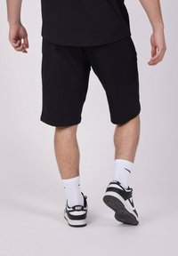 Pantalones cortos de algodón negros con un corte relajado, que llegan a la mitad del muslo, combinados con calcetines deportivos blancos y zapatillas negras con un acento blanco.