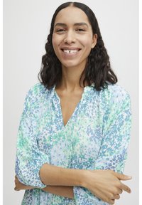Blusa floral en tonos de verde y azul. Tejido suave y ligero con escote en V y mangas fruncidas. El patrón presenta pequeñas flores y hojas.