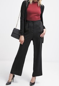 Pantalon noir taille haute avec plis, associé à un haut bordeaux ajusté et un cardigan noir. Des talons noirs et un petit sac à main noir complètent le look.