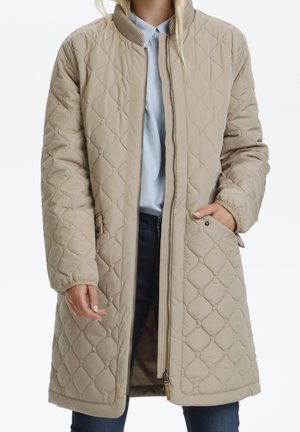 Beige quiltet lang frakke med opretstående krave, trykknap- og lynlåslukning, sidelommer og ribstrikkede ærmekanter; glat tekstur og diamantmønster.