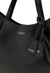 Borsa a spalla nera in ecopelle con finitura testurizzata, dotata di accenti dorati con il logo e due etichette decorative, una delle quali a forma di triangolo.