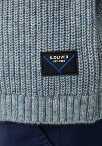 Gestrickter Pullover in Hellblau und Grau, mit einem gerippten Muster und einem schwarzen Patch mit blauer und weißer Schrift sowie Emblem.