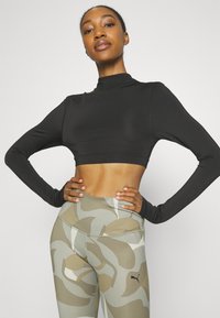 Top negro de manga larga recortada combinado con leggings de talle alto con un patrón de camuflaje en tonos beige y verde suave.
