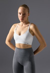 Weißer Sport-BH mit verstellbaren Trägern und V-Ausschnitt, kombiniert mit hoch taillierten grauen Leggings, die eine glatte Textur und keine Muster aufweisen.