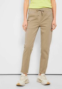 Beiga bomullsmixbyxor med elastisk dragsko i midjan, sidofickor och tapered ben-design, kombinerade med kraftiga ljusa sneakers.