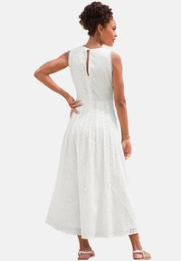 Weißes knielanges Kleid aus Spitzstoff mit floralen Ausschnitten, kurzen Ärmeln und einem Schlüsselanzugsdesign auf der Rückseite.