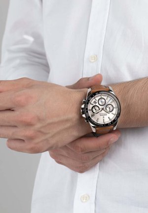 Montre chronographe avec un cadran argenté, une lunette noire et un bracelet en cuir brun. Comprend trois sous-cadrans et un boîtier en métal poli.