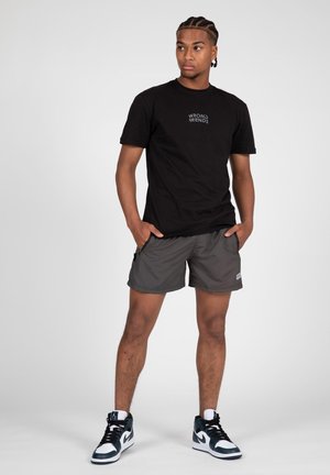 Camiseta de algodón negra con el logo "WRONG FRIENDS", pantalones cortos deportivos grises y zapatillas negras con detalles blancos, exhibidos sobre un fondo sencillo.