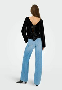 Top lungo a maniche con velluto nero, con uno scollo a V profondo sul retro e dettaglio a fiocco. Abbinato a jeans a gamba larga azzurri e stivaletti neri con tacco.