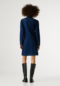 Tumši zilas džinsa kleitas krekls ar garām piedurknēm, pogu aprocēm un taisnu griezumu. Izceļas ar aizmugurējo jostu un redzamām šuvju detaļām.