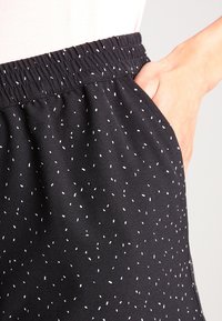 Černé šortky z měkkého materiálu s elastickým pasem, bočními kapsami a bílým vzorem rozptýlených teček.