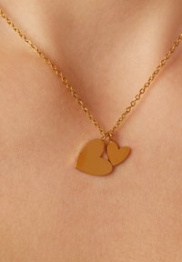 Halskette in Goldoptik mit zwei Herzanhängern, einem größeren und einem kleineren, mit einer glatten Oberfläche und einem miteinander verbundenen Kettendesign.