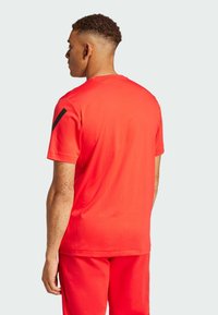 Camiseta roja de manga corta con cuello redondo, textura suave y acento negro en el hombro. Combina con pantalones rojos a juego.