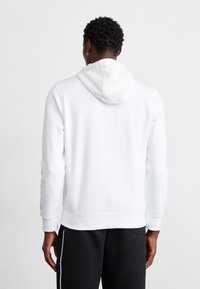 Vit hoodie med dragsko i huvan, ribbade ärmar och en avslappnad passform, parat med svarta byxor med kontrasterande sidostripes.