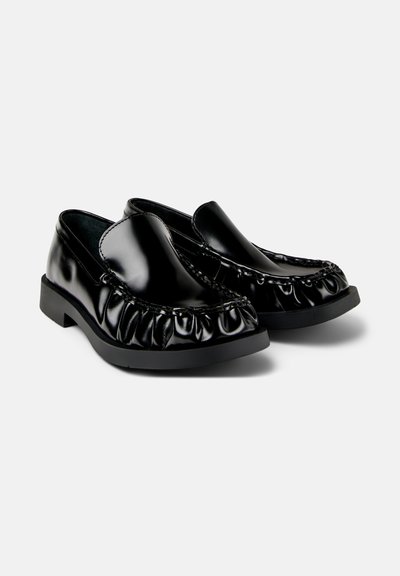 Pair of glossy black slip-on loafers with ruched detailing around the toe and black flat rubber soles on a white background.