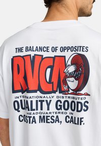 Camiseta de algodón blanca con gráficos en rojo y azul marino, incluyendo "RVCA" y un personaje de dibujos animados, con texto que detalla la ubicación y la calidad.