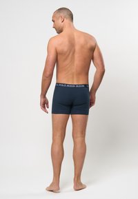 Tengerészett kék boxer alsónadrág, simulékony fazonnal és rugalmas derékpánttal, amelyen a "U.S. Polo Assn." felirat fehér színben látható. A textúra simának tűnik.