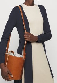 Gebreide jurk met kleurvlakken in marineblauw en crème, ronde halslijn en lange mouwen. Bruine leren bucketbag met verstelbare riem en trekkoordsluiting.