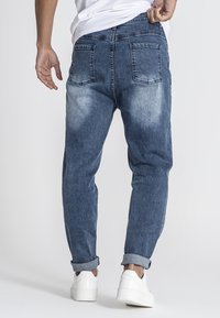 Jeans de mezclilla, con un lavado azul deslavado, diseño de pierna recta, bolsillos traseros y puños enrollados, combinados con unas zapatillas blancas.