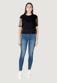 Cropped top nero con maniche in tulle nero e ricami ondulati all'orlo, abbinato a jeans skinny blu e sneakers bianche.