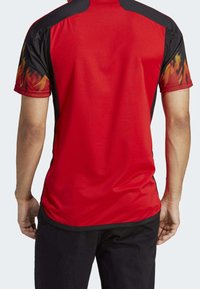 Camiseta deportiva roja con detalles en negro y mangas cortas. Presenta un patrón de llamas en las mangas, hecha de un material que absorbe la humedad.