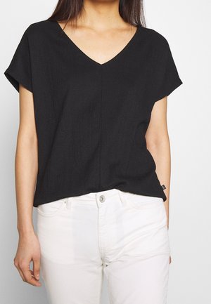 Haut noir à manches courtes avec un col en V, fabriqué en tissu texturé. Un style simple est associé à un pantalon blanc pour un contraste.