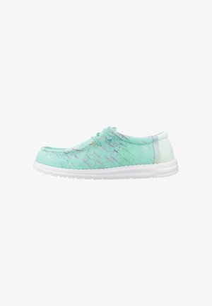 Zapato casual tipo slip-on en color turquesa claro con suela blanca y sutiles acentos multicolores, visto de lado sobre un fondo blanco.