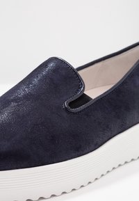 Námornické semišové nazouvací boty s elastickými bočními akcenty, bílou texturovanou podrážkou a hladkým podšívkem. Vyznačují se zaobleným tvarem a minimalistickým designem.