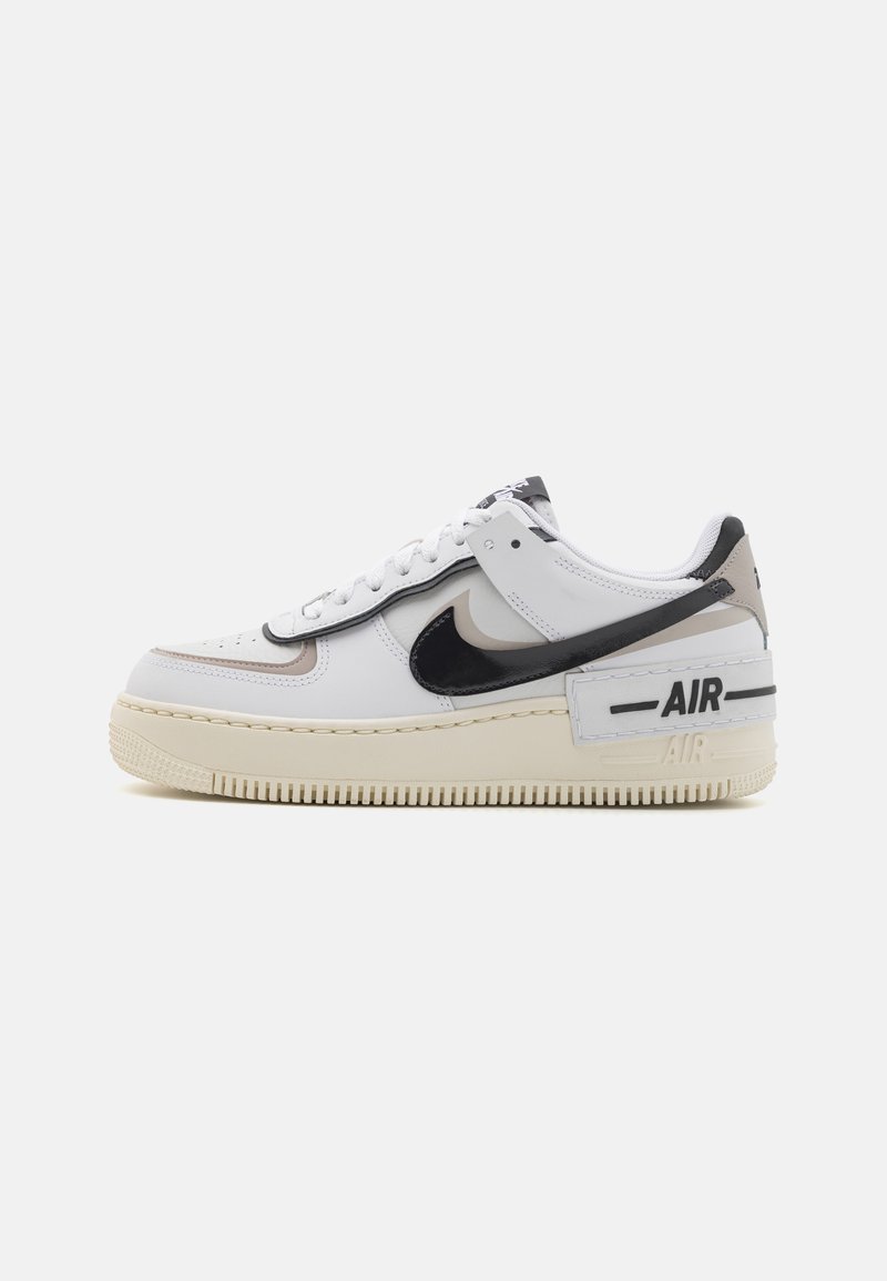 Fehér sneaker fekete és bézs kiegészítőkkel, sima bőr felsőrésszel, kerek orral, fűzős záródással és texturált gumitalppal.
