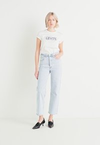 Biela tričko s fialovým logom Levi's, svetlo modré vysoké rifle a čierne špicaté poltopánky. Jednoduchý strih a voľný strih po celom oblečení.