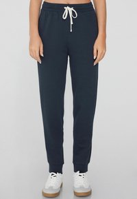 Pantalones jogger azul marino hechos de tela suave, con una cinturilla elástica y cordón blanco, además de puños acanalados. Combinados con zapatillas blancas.