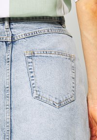 Jupe en denim bleu clair avec une poche arrière à surpiqûres contrastantes, texture légèrement délavée et silhouette classique en A.