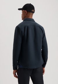 Cămașă din fleece de culoare albastru închis, cu guler clasic, manșete cu nasturi și hem curbat. Dispune de un material texturat și un design simplu.