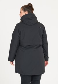 Svart, vattentät parka med huva, med avslappnad passform, långa ärmar och rak silhuett. Slät textur med minimal detalj.