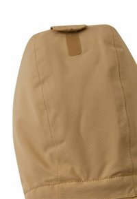 Beige Oberbekleidung mit Kapuze, die eine glatte Textur, verstärkte Nähte und einen gewebten Stoffverschluss an der Oberseite für eine sichere Befestigung aufweist.