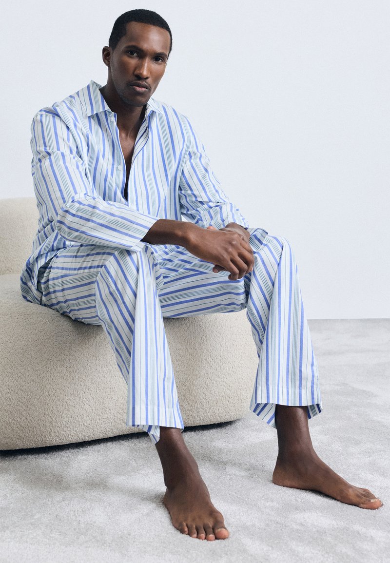 Set de pijama ușor, cu dungi albastre și albe, având o cămașă cu guler și închidere cu nasturi, împreună cu pantaloni confortabili, confecționați dintr-un material moale.