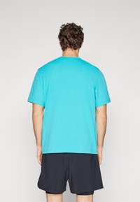 T-shirt turquoise à col rond en tissu léger, avec des manches courtes et une coupe décontractée, porté avec un short sombre.
