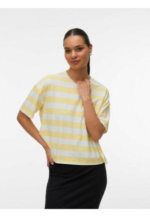 Kvinde med mørkt hår i hestehale iført perleøreringe, en gul- og hvidstribet kortærmet skjorte og et sort skørt mod en hvid baggrund.