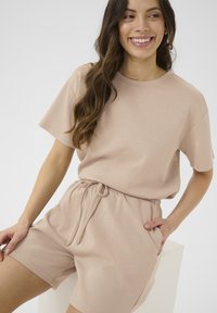 Completo loungewear beige chiaro composto da una t-shirt a maniche corte e pantaloni corti con vita elastica e cordoncino. Tessuto morbido con una texture liscia.