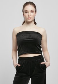 Haut court noir sans manches en velours lisse, avec un ourlet droit. Associé à un pantalon en velours noir avec des poches latérales.