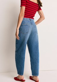 Jean taille haute bleu clair, à la coupe décontractée, avec deux poches arrière et une texture délavée, associés à des chaussures rouges à enfiler.