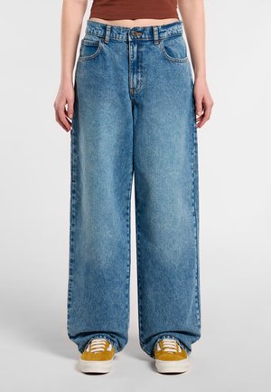 Jeans in denim azzurro chiaro, a gamba larga con vita alta, dotati di cinque tasche e cuciture a contrasto. Abbinati a sneakers gialle.