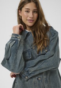 Jeansjacke mit hellblauer Waschung und gesprenkelten Details, Knopfverschlüssen, zwei Brusttaschen und weit geschnittenen Ärmeln.