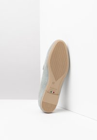 La suola beige in gomma con motivo è visibile sul fondo della scarpa grigia in suede, con il logo del marchio e un dettaglio della bandiera italiana, angolata su uno sfondo bianco.
