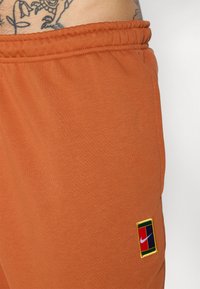 Oranžové bavlnené šortky s elastickým pásom a malou vyšívanou multikolórovou nášivkou Nike na boku. Mäkkučká textúra.