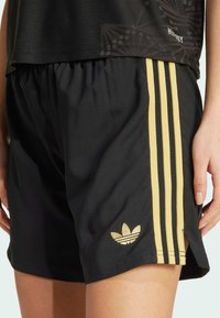 Shorts sportivi neri realizzati in tessuto leggero con strisce dorate sui lati e logo dorato. Presenta tasche a filo e una vestibilità comoda.